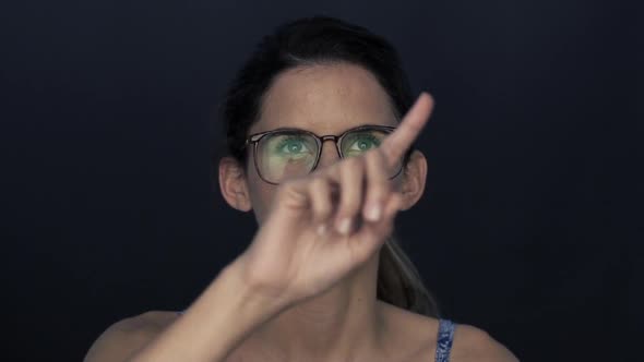 Woman wearing glasses, looking up and gesturing as if using touch screen