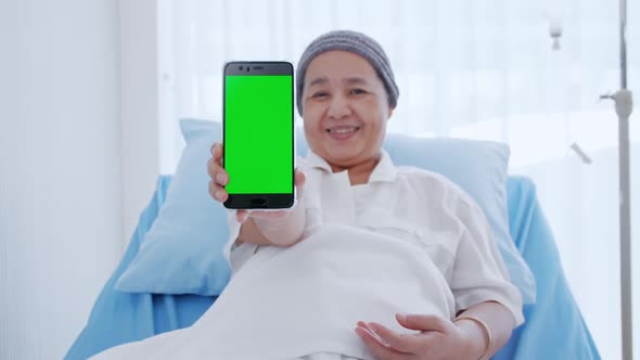 An elderly woman with cancer sitting on bed and showing some information on her smart phone.