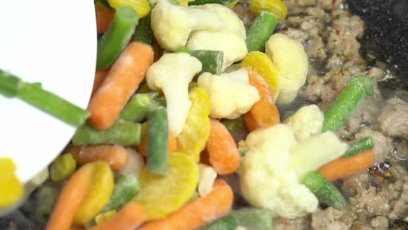 Adding frozen vegetables to minced meat in a pan on stove slow motion. Frying