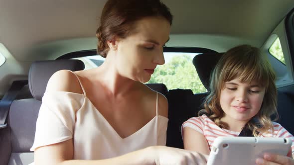 Mother and daughter using digital tablet in the back seat of car