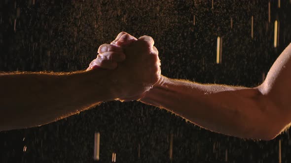 Handshake of Two Muscular Men on a Black Background Among Raindrops and Many Splashes. Slow Motion