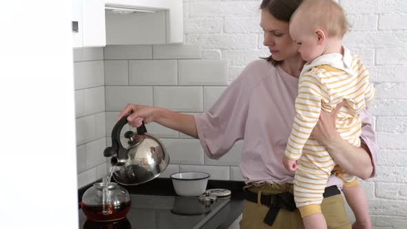 Young Mother Holding Baby Girl in Arms Preparing Food Together in Kitchen