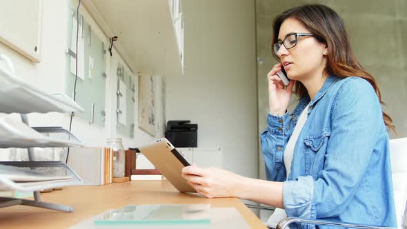 Female executive using digital tablet while talking on mobile phone