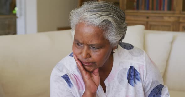 Close up of worried african american senior woman with hand on chin sitting on the couch at home