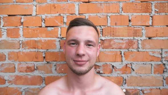 Portrait of Smiles Young Guy with Naked Torso Standing on Red Brick Wall Background