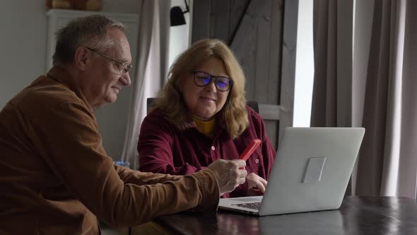 two elderly people surfing internet on laptop computer at home.