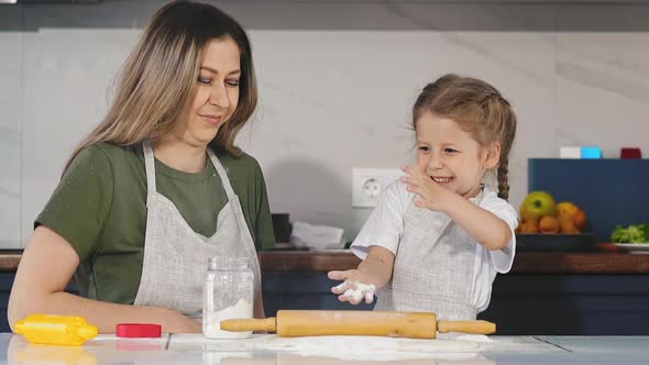 Daughter Plays with Flour Cooking with Young Mother at Table