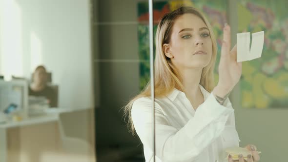 young businesswoman sticking sticky notes on glass at office