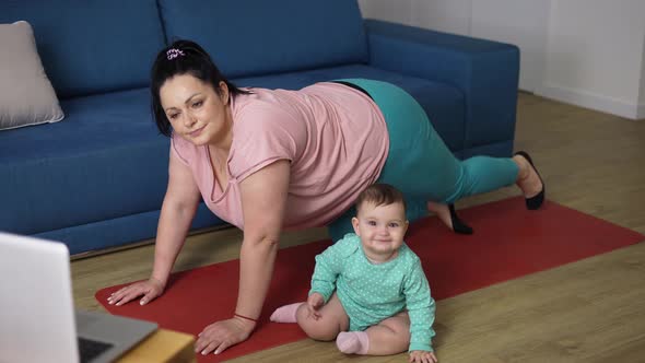 Overweighted Woman Doing Exercises Online From Laptop with Little Baby Next to Her