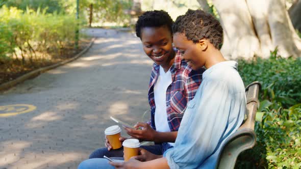 Twin sisters using mobile phone in the park 4k