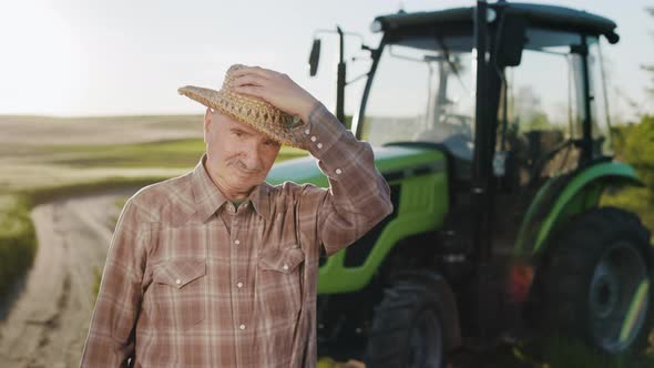 The Old Farmer is Putting on His Straw Hat and Looking at the Camera
