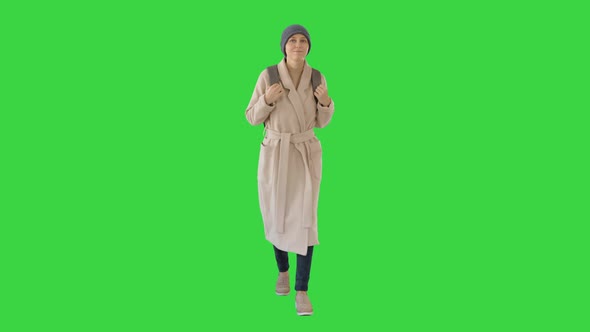 Young Woman Wearing Coat and Backpack Walking on a Green Screen, Chroma Key.