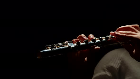 Female fingers playing the flute, close-up. Thin female fingers move on the keys of a chrome flute