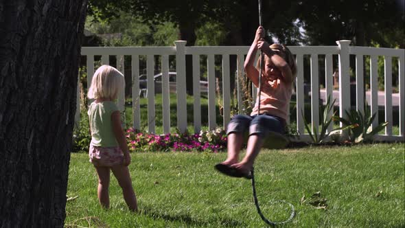 Slow motion handheld shot of a child swinging on a tree swing while another one looks on