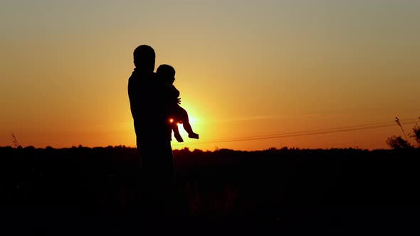 Caring Father Holds the Baby in Her Arms and Kisses Him Unrecognizable Silhouette at Sunset