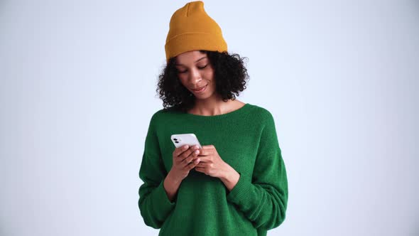 Positive curly-haired woman wearing hat typing by phone