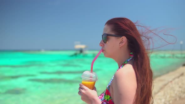 Young Woman Drinking a Fruit Cocktail on the Shore of the Azure Sea