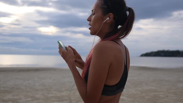 Sport Woman With Smartphone Exercises on Beach After Jogging