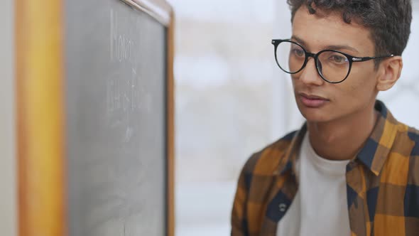 Portrait of Concentrated Teen Student in Eyeglasses Writing on Blackboard in Classroom