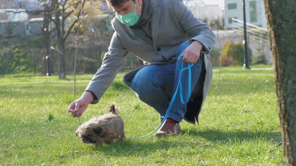 Man in Mask Squats and Holds Leash with Adorable Small Dog