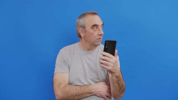 Happy Senior Elderly Man Holding Smart Phone Watching Mobile Video Calling Online Looking at Screen.