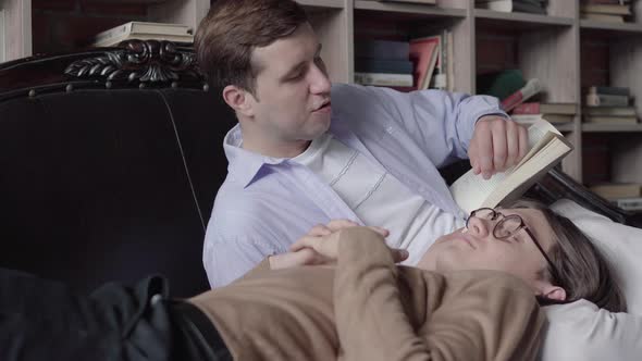 Concentrated Brunette Man Reading for Gay Partner in Library. Portrait of Loving Caucasian Guy Lying