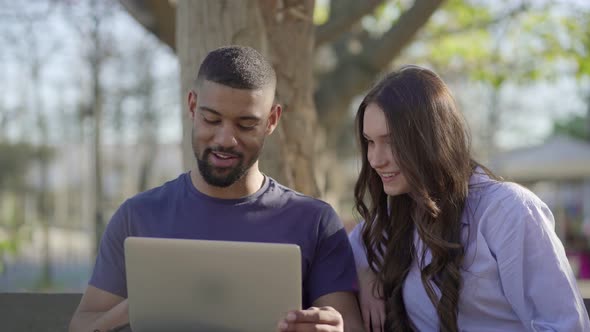 Young Man and Pretty Woman in Park Looking at Laptop, Discussing 