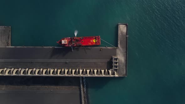 Red cargo ship moored at pier of Tazacorte harbor in La Palma island. Aerial top-down sideways