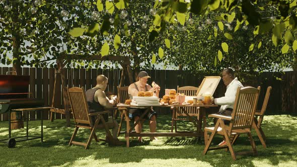 Garden party. Friends eating hot dogs and hamburgers setting around the table.