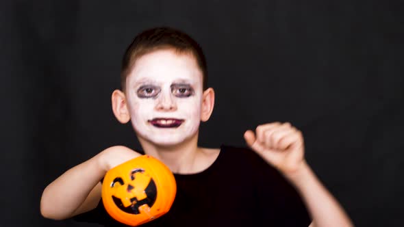 cheerful caucasian boy 8 years old in a halloween costume with monster make-up dances holding a pump