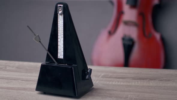 A black vintage metronome beats the rhythm while standing on the table, a cello is lying behind