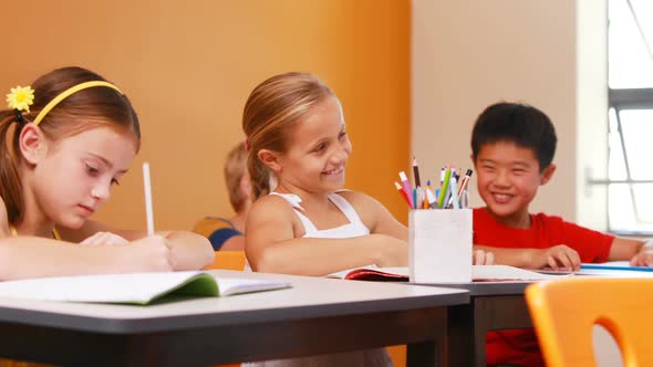 Schoolgirl whispering into her friends ear in classroom