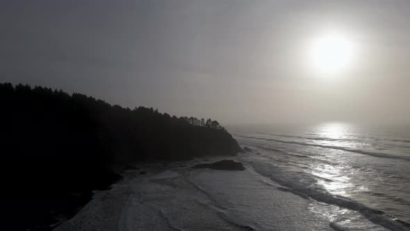 Golden hazy sunlight reflects off rhythmic ocean waves and rugged Washington coastline, aerial