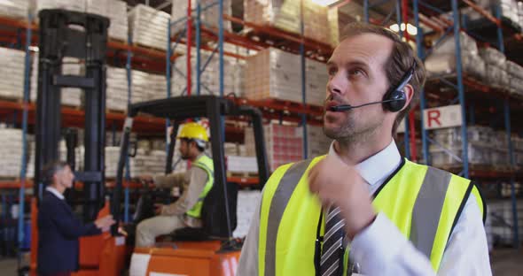 Male warehouse manager talking with headset in loading bay 4k