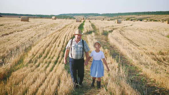 Grandfather and Granddaughter Walking Across the Field with Haystacks