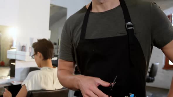 Male hairdresser holding scissor, comb and brush in salon