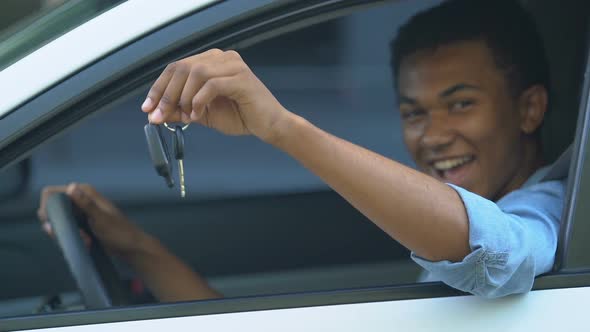 Happy black male teenager on driver place showing car keys