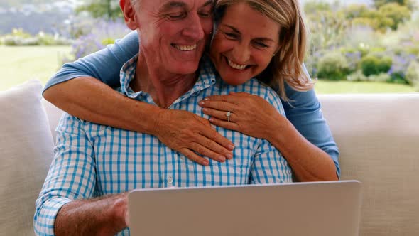 Smiling senior woman embracing a man in living room while using laptop