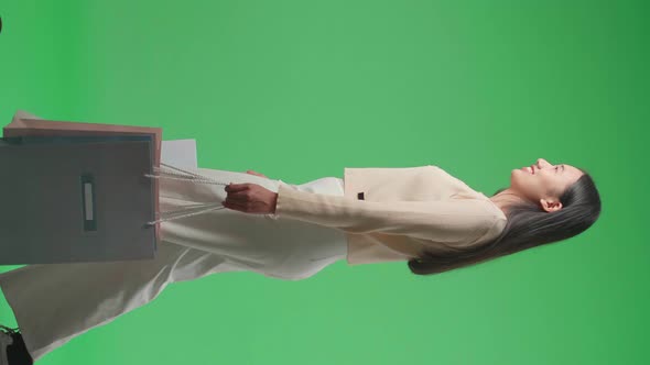 Side View Of An Asian Shopping Woman With Shopping Bags Smile And Walking In Front Of Green Screen