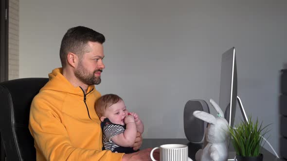 Man working on a computer with a baby in his arms