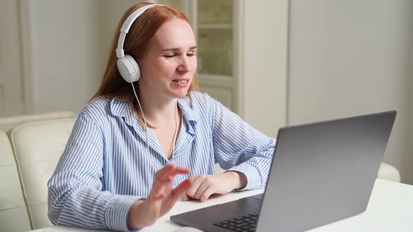 Woman with Headphones Works at Home on a Laptop Leads a Lesson or Webinar