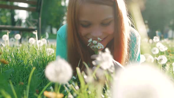 Beauty Girl lying on dandelions meadow and smelling flowers. Beautiful Spring Young Woman with red h