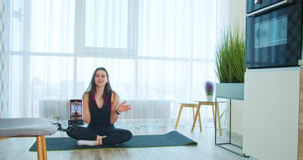 Young Woman is Sitting on a Yoga Mat and Recording a Video on Her Phone