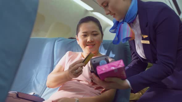 Onboard product purchasing, Asian woman sit in airplane use credit card buy gift from air hostess.