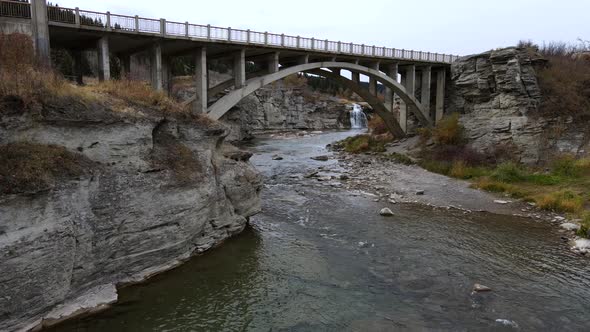 Still aerial slo-mo footage of crowsnest river flowing underneath a large bridge in rural Alberta du