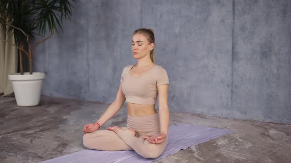 Young Female Yoga Coath Sitting in Lotus Pose or Padmasana with Closed Eyes and Holding Her Hands in