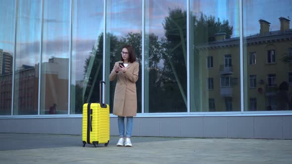 Attractive Young Woman with a Suitcase Got Lost. The Girl Looks at the Map on the Phone and Looks