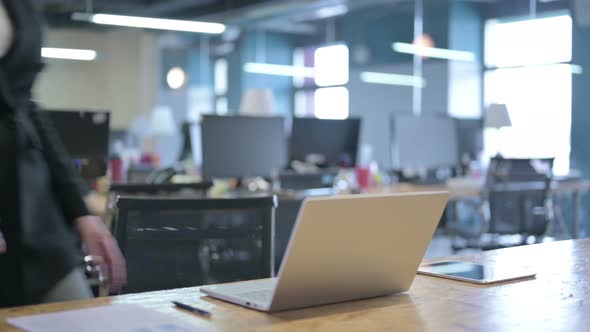 Serious Middle Aged Businesswoman Coming Back and Sitting on Table with Laptop