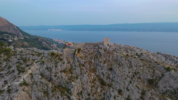 Aerial: Starigrad Fortress on Adriatic clifftop, Omis Croatia, sunset arc shot