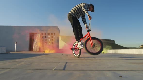 BMX rider on a rooftop jumping and using smoke grenades